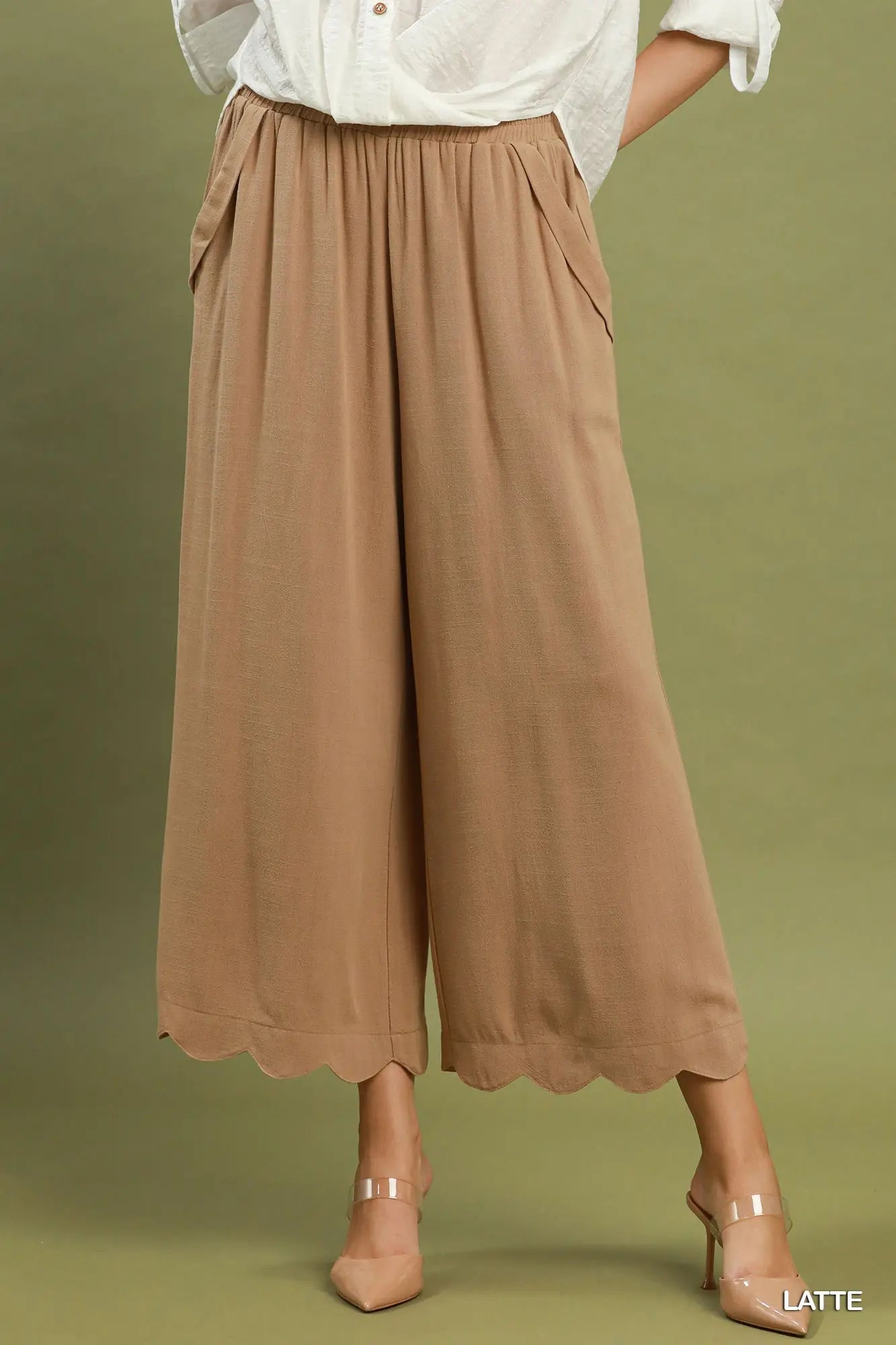 Person wearing brown wide-leg pants and a white shirt on a green background