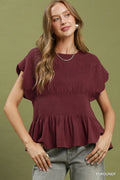 Woman wearing a burgundy peplum top against a green background