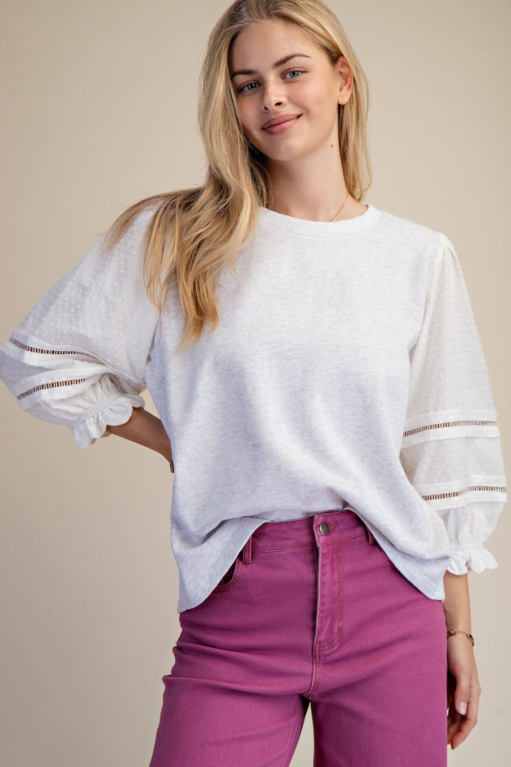 Woman wearing a white blouse with lace details and pink pants on a beige background