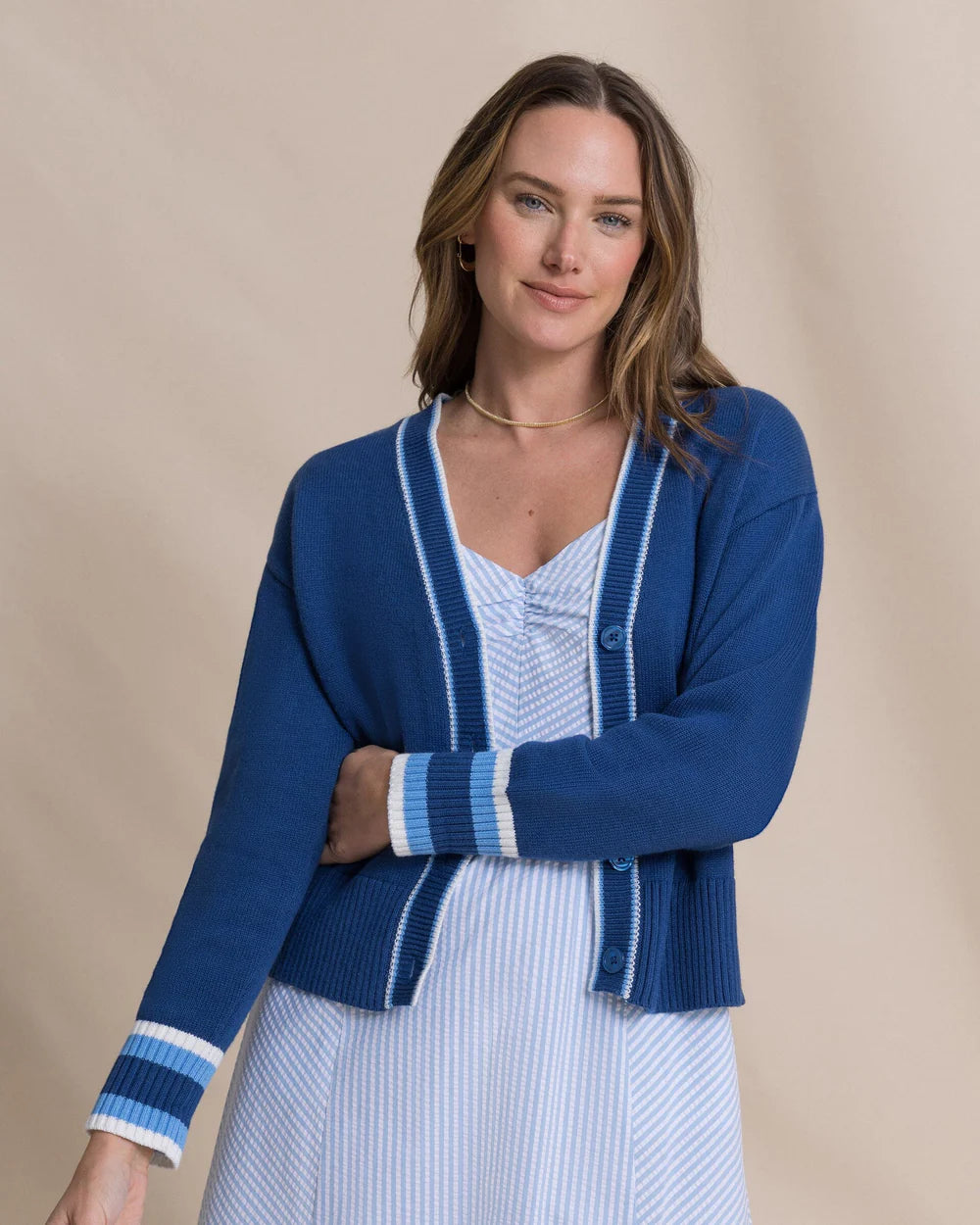 Woman wearing a blue cardigan over a white dress on a beige background