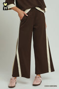 Brown wide-leg pants with white stripes worn by a person on a light gray background