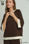 Woman wearing a brown and beige top with a visible brand logo on a light gray background