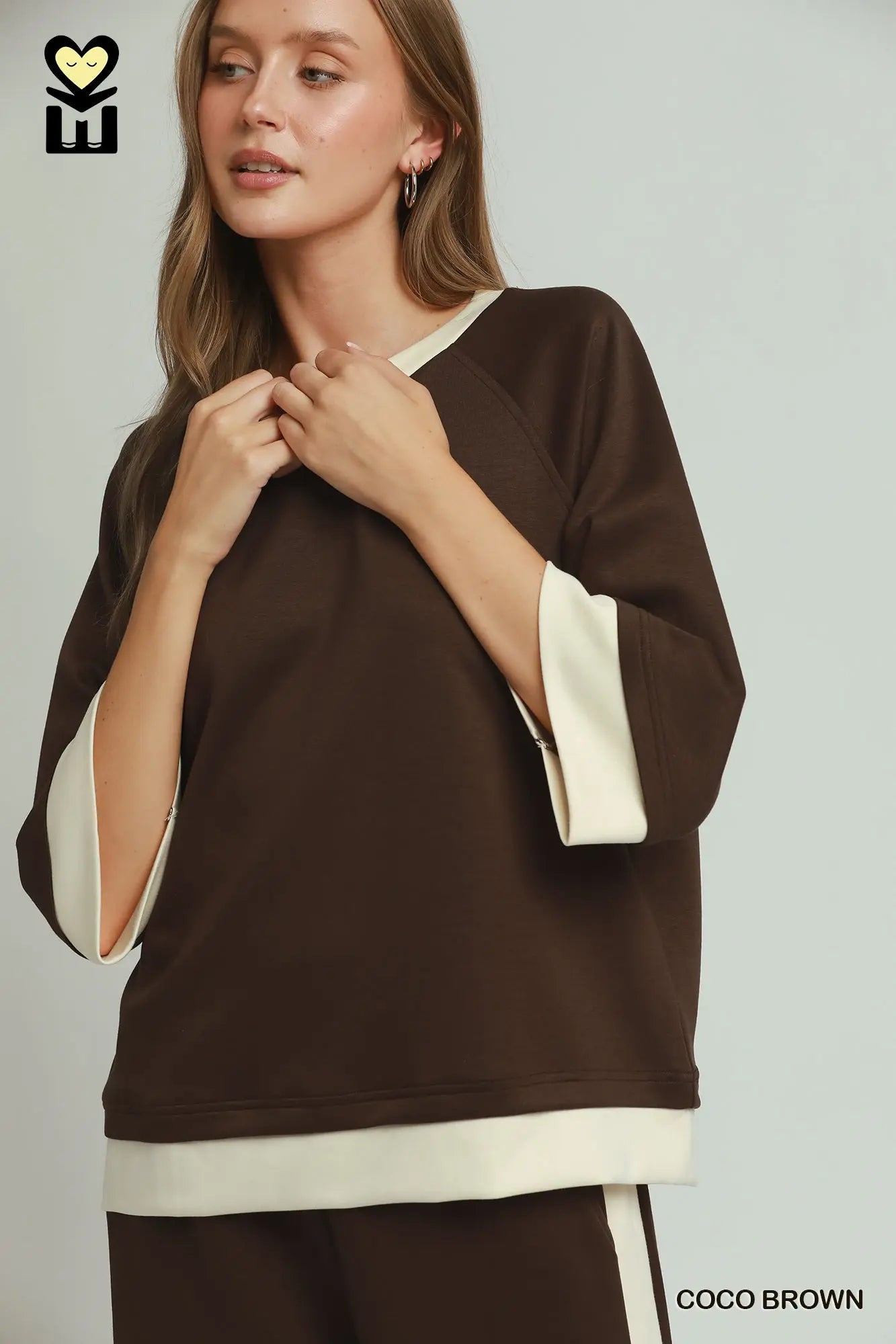 Woman wearing a brown and beige top with a visible brand logo on a light gray background
