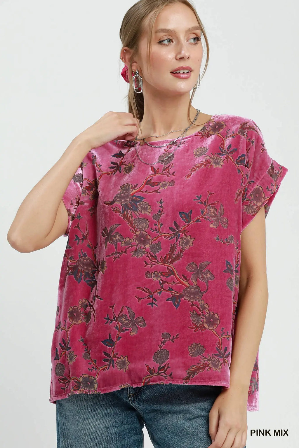 A woman wearing a pink short-sleeve top with a dark floral pattern, paired with blue jeans, against a plain white background.