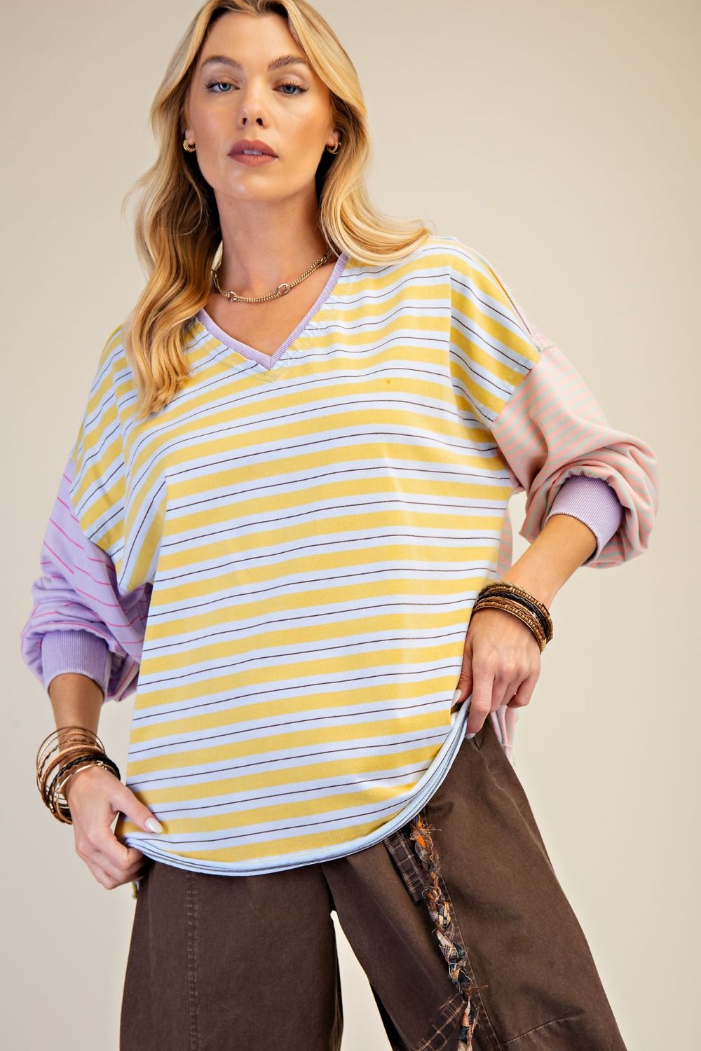 Woman wearing a yellow and purple striped shirt with brown pants on a beige background