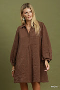 A woman modeling a brown textured long-sleeve mini dress against a solid olive green background. The word 'MOCHA' is printed in white in the bottom right corner.