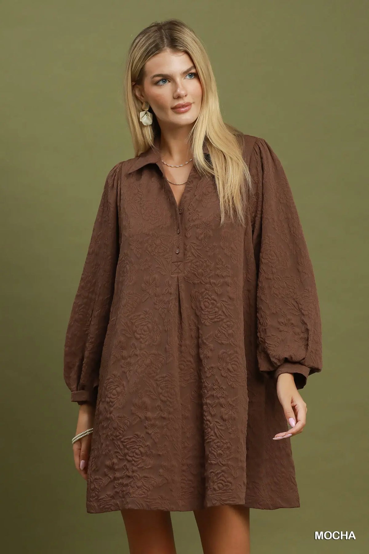 A woman modeling a brown textured long-sleeve mini dress against a solid olive green background. The word 'MOCHA' is printed in white in the bottom right corner.