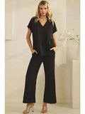 Woman wearing a black outfit with wide-leg pants against a neutral background