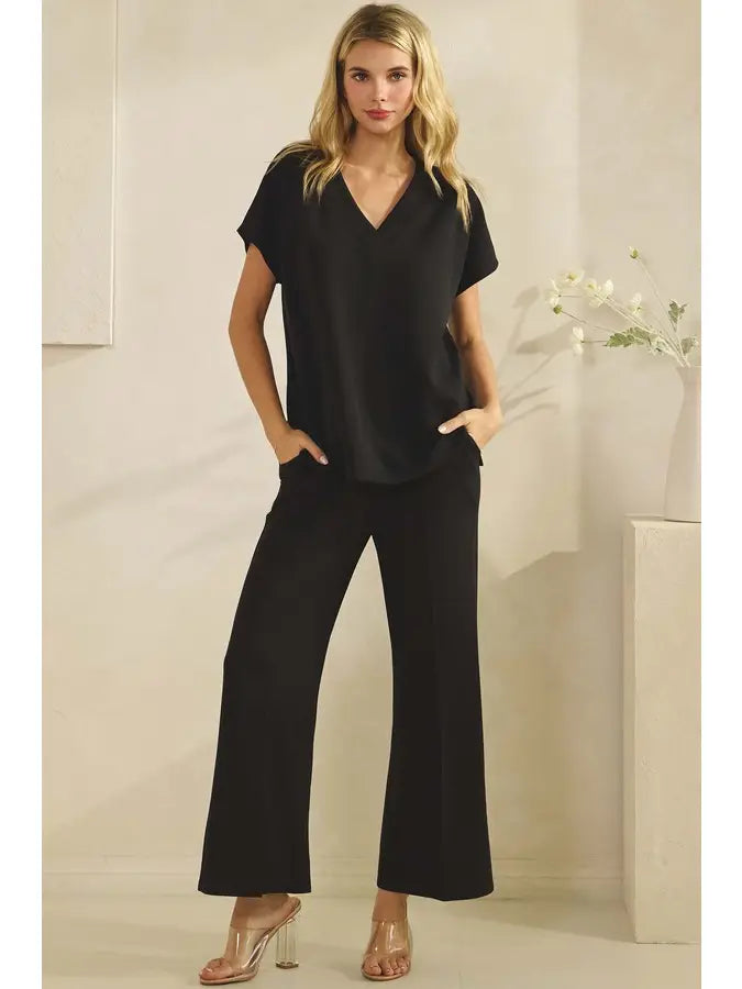 Woman wearing a black outfit with wide-leg pants against a neutral background