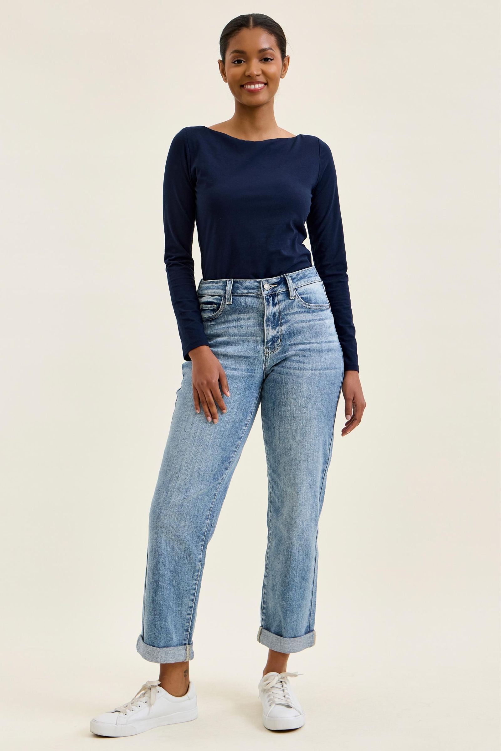 Woman wearing a navy long-sleeve top and light blue jeans on a beige background