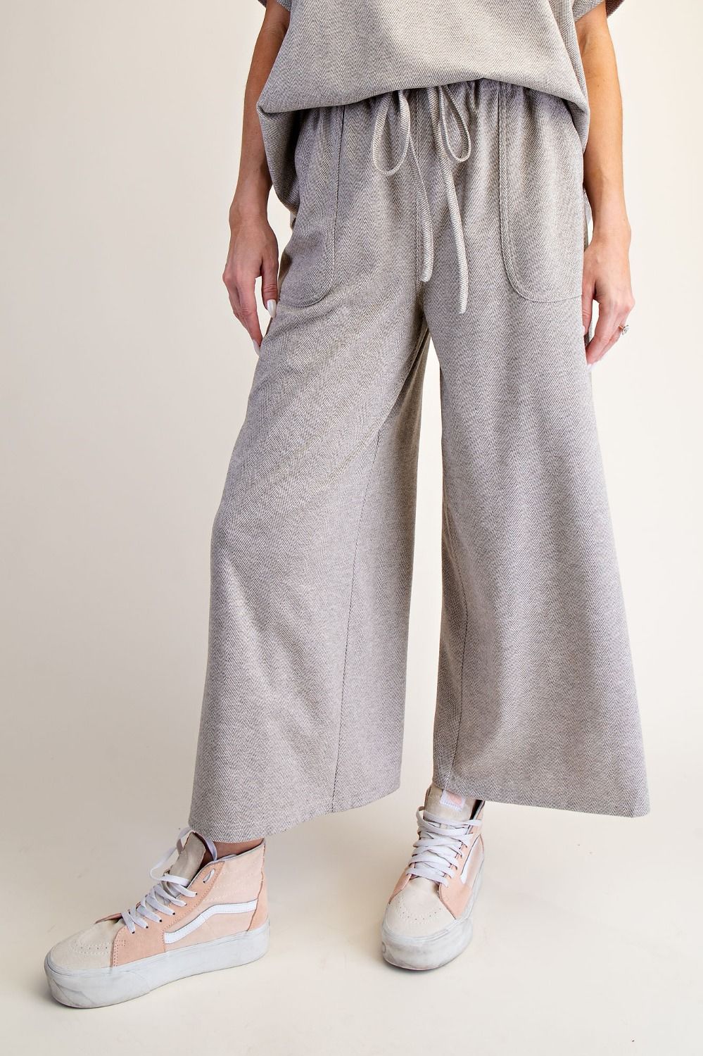 Person wearing gray wide-leg pants and light-colored sneakers on a plain background