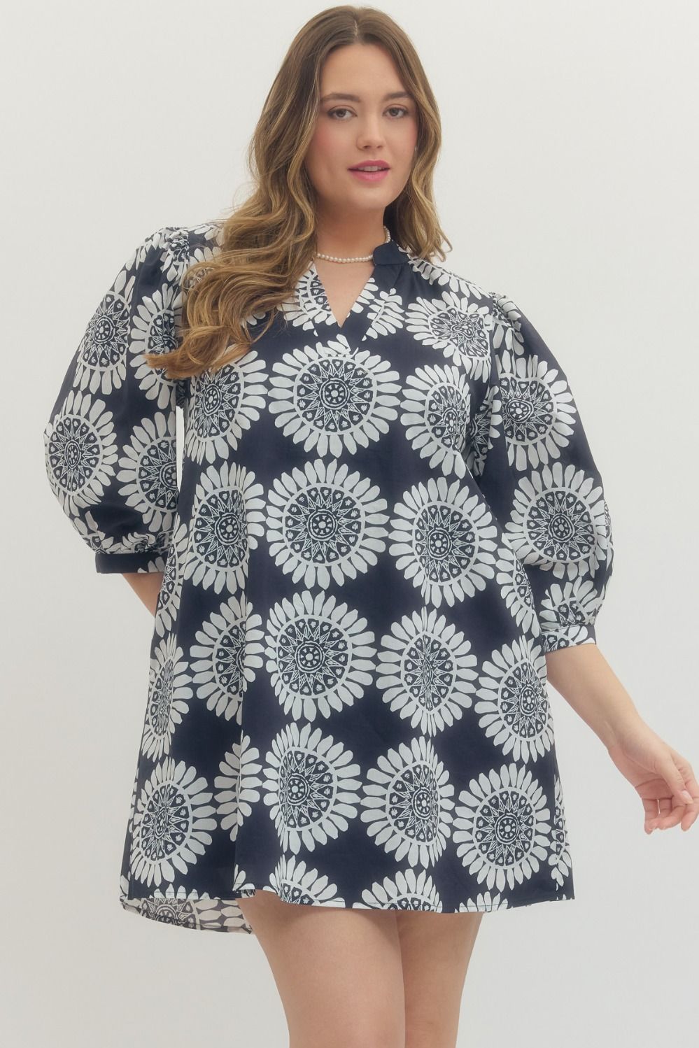 Woman wearing a navy dress with white floral pattern on a plain background