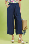 Person wearing navy wide-leg pants with a colorful top and beige bag on a green background