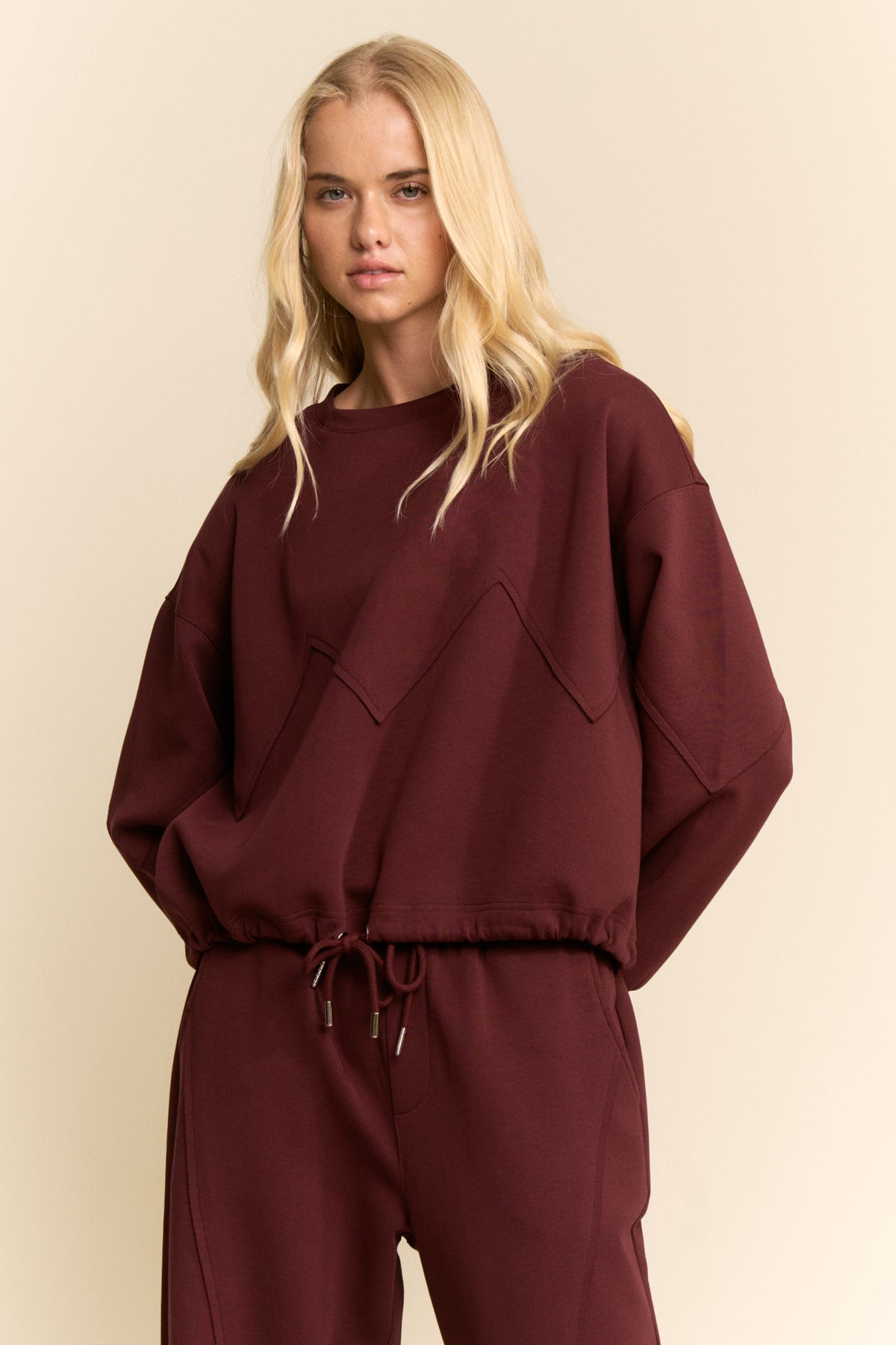 Woman wearing a burgundy tracksuit against a beige background