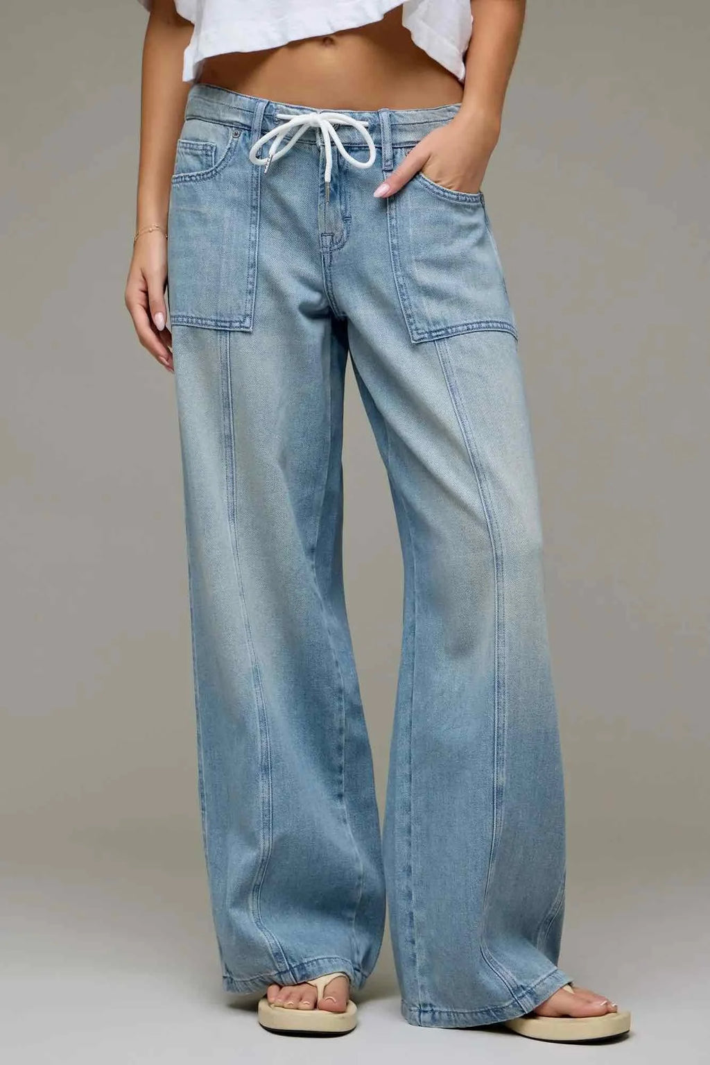 A person wearing light-wash wide-leg denim jeans with a white drawstring waist, shown from the waist down against a plain light gray studio background.