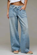 A person wearing light-wash wide-leg denim jeans with a white drawstring waist, shown from the waist down against a plain light gray studio background.