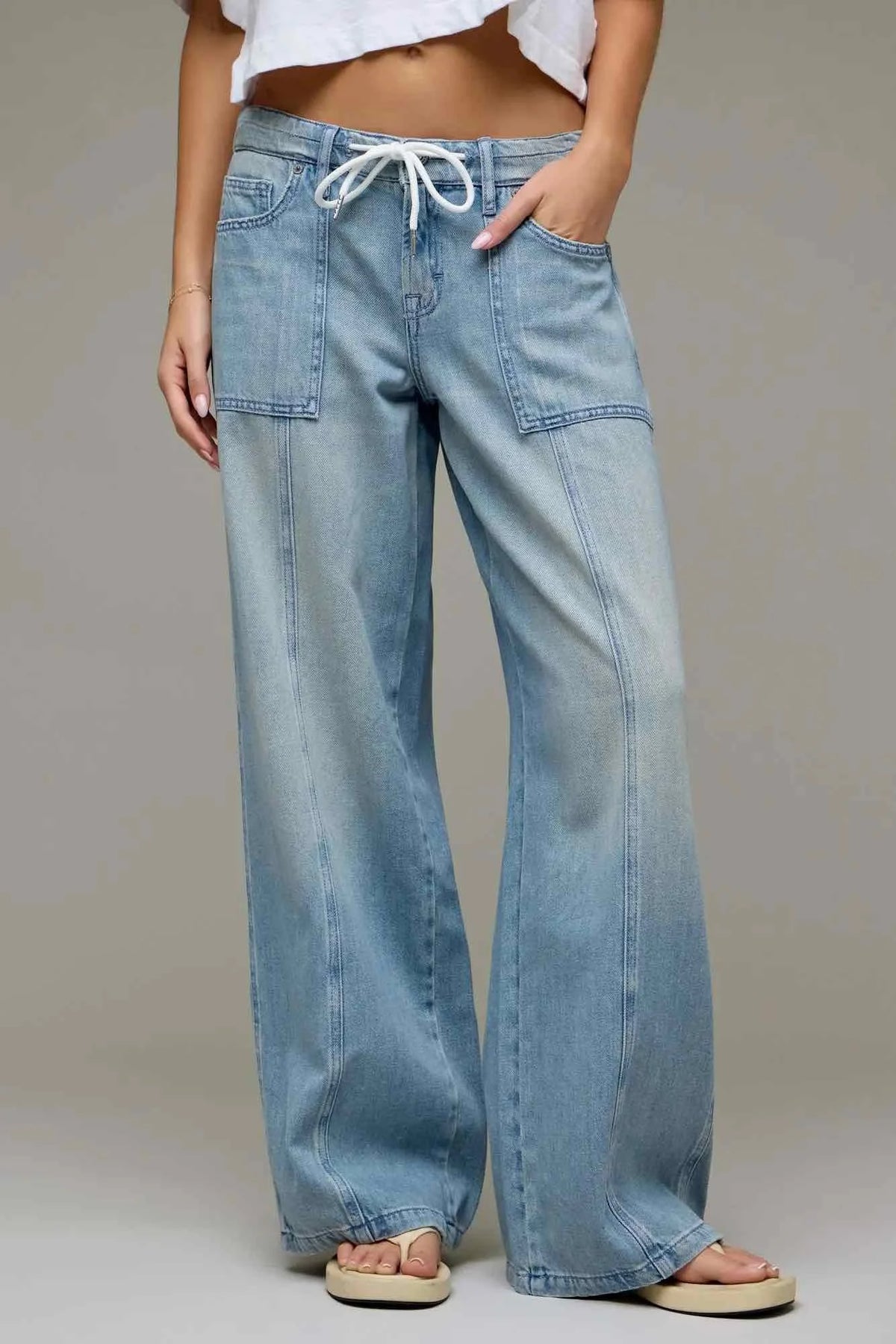 A person wearing light-wash wide-leg denim jeans with a white drawstring waist, shown from the waist down against a plain light gray studio background.