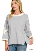 A woman wearing a heather gray long-sleeve top with cream-colored trim and a star patch on one sleeve, paired with blue jeans against a white background.