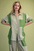 A woman modeling a patchwork button-up shirt and matching pants in green and beige plaid fabrics, posed against a solid light green studio background.
