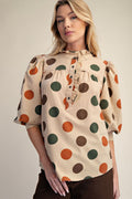 Woman wearing a beige blouse with colorful polka dots on a plain background