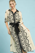 Woman wearing a long, patterned dress with a black belt against a light blue background