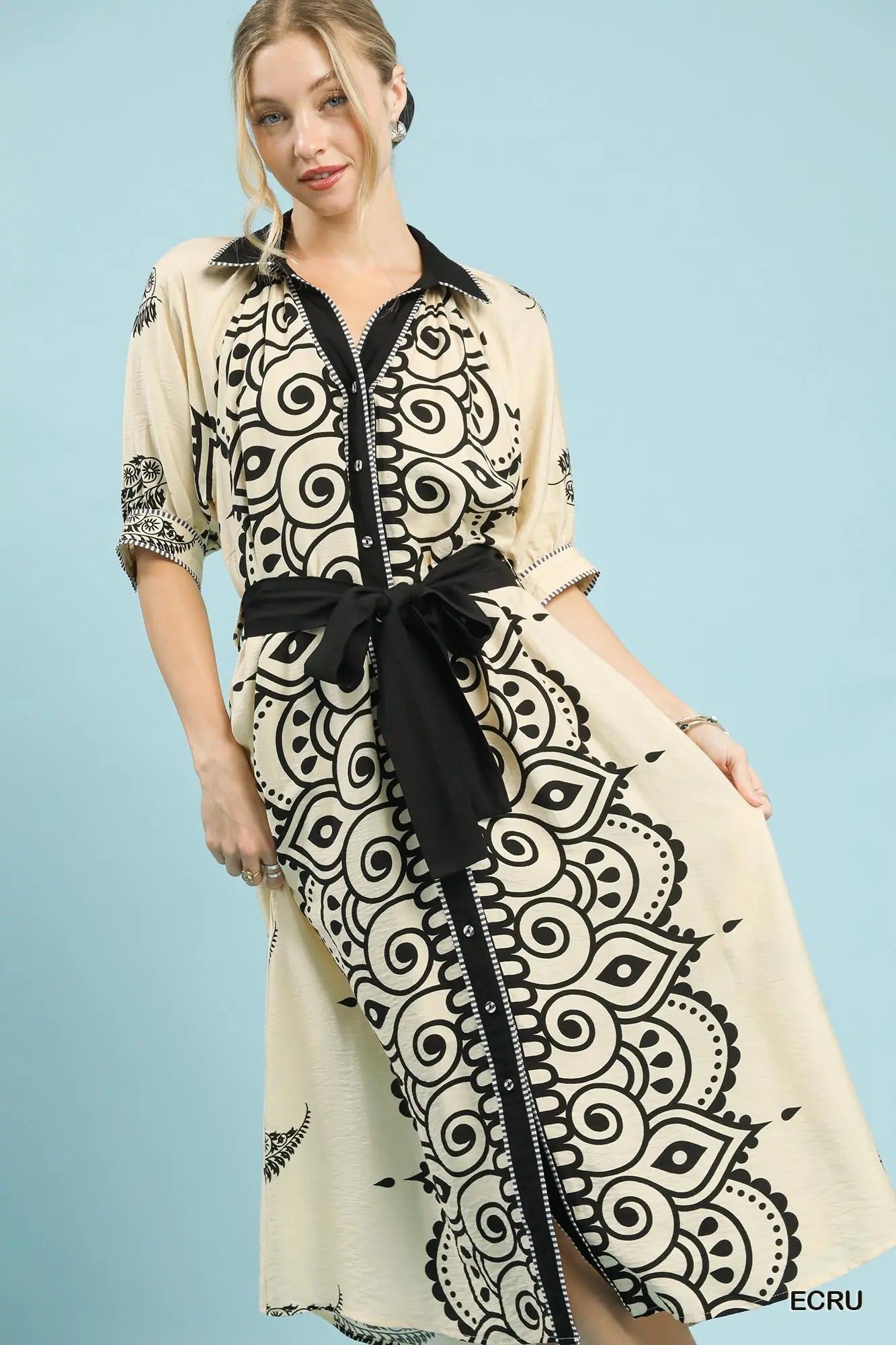 Woman wearing a long, patterned dress with a black belt against a light blue background