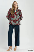 Woman wearing a patterned blouse and dark pants on a white background