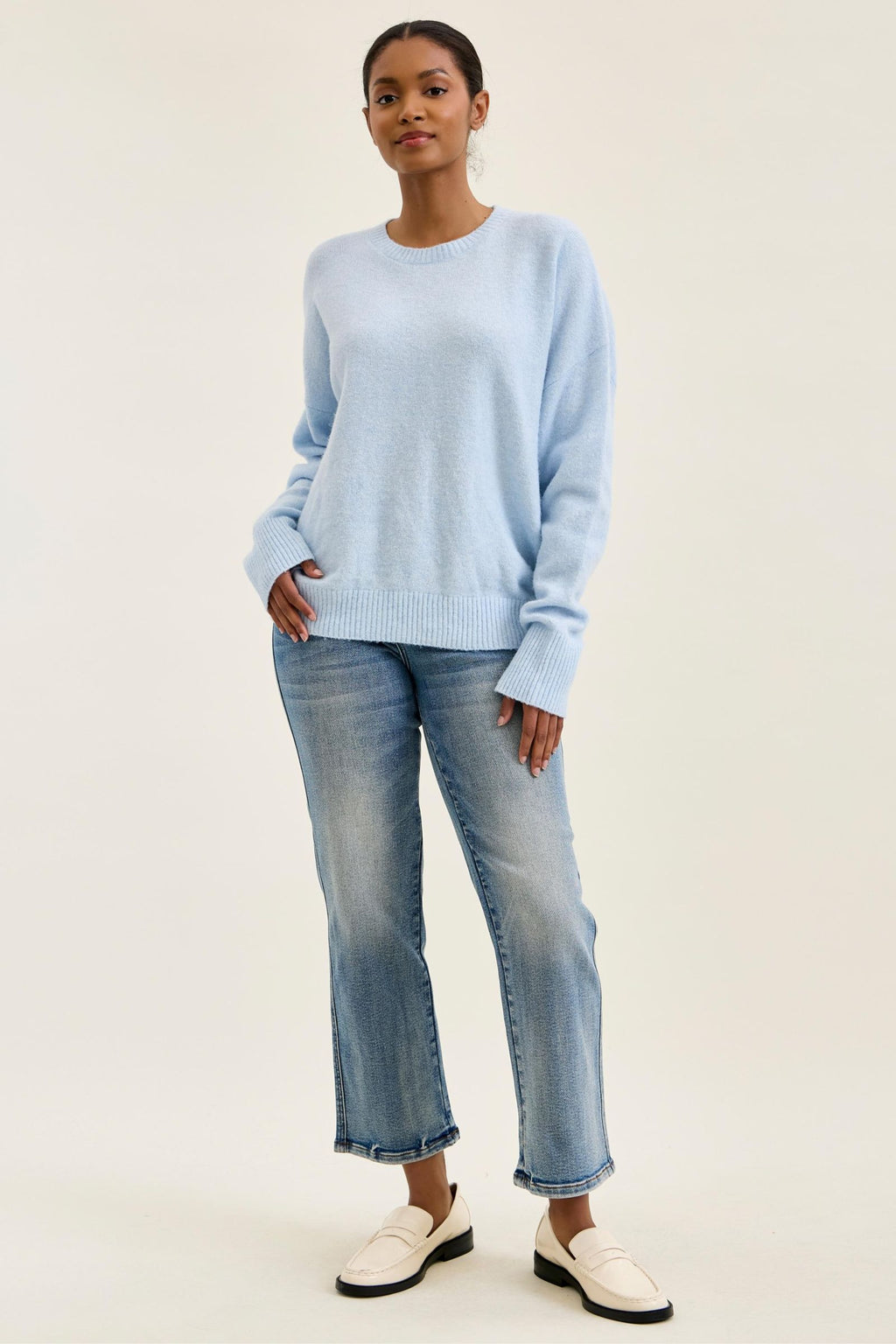 Woman wearing a light blue sweater and jeans on a white background