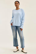 Woman wearing a light blue sweater and jeans on a white background