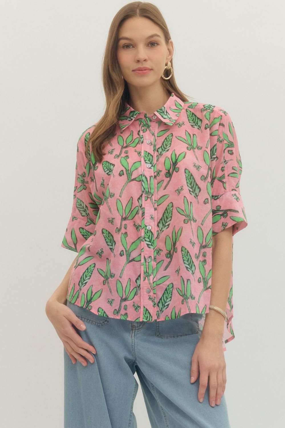 Woman wearing a pink blouse with green leaf pattern and blue jeans on a white background