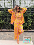 Woman wearing a yellow and pink floral outfit standing outdoors with greenery in the background