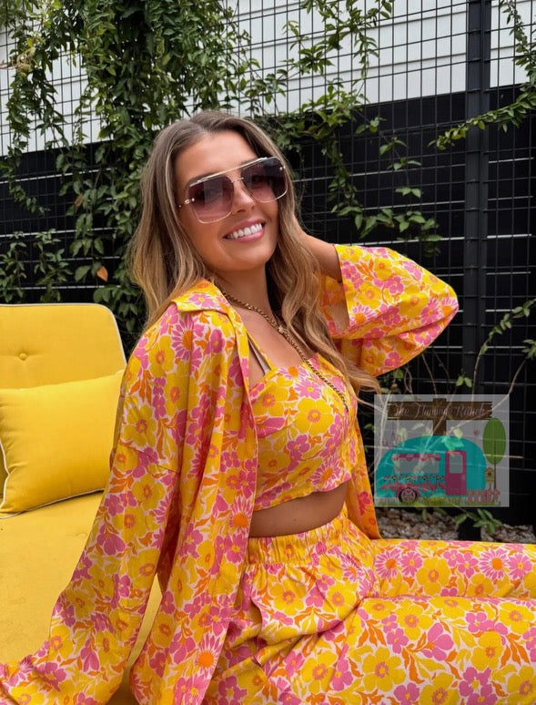 Woman in a yellow and pink floral outfit sitting on a yellow chair outdoors.