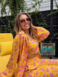 Woman in a yellow and pink floral outfit sitting on a yellow chair outdoors.