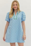 Woman wearing a light blue dress with green polka dots on a plain background