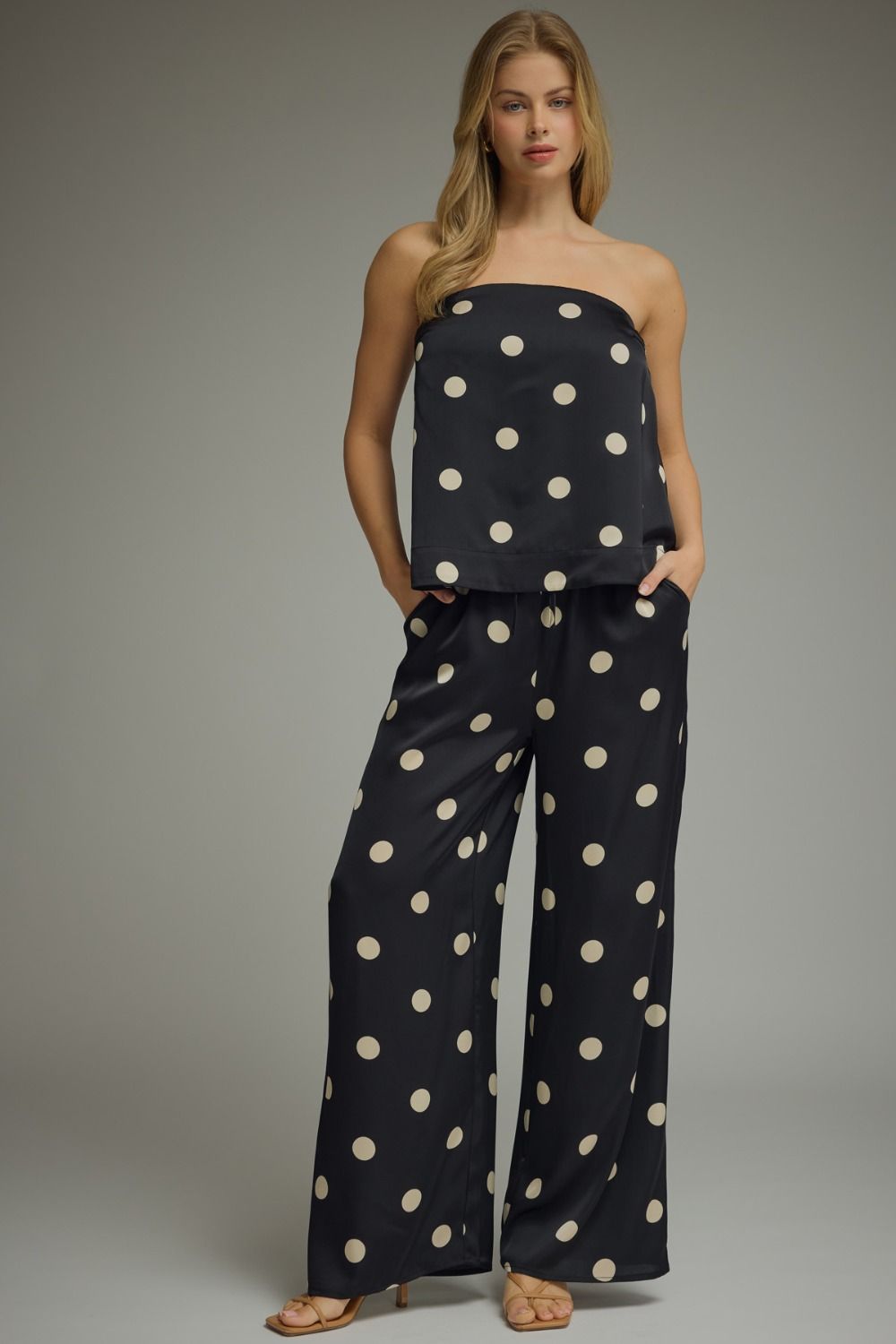 Woman wearing a black strapless top and wide-leg pants with white polka dots on a gray background