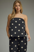 Woman wearing a black strapless top and pants with white polka dots on a gray background
