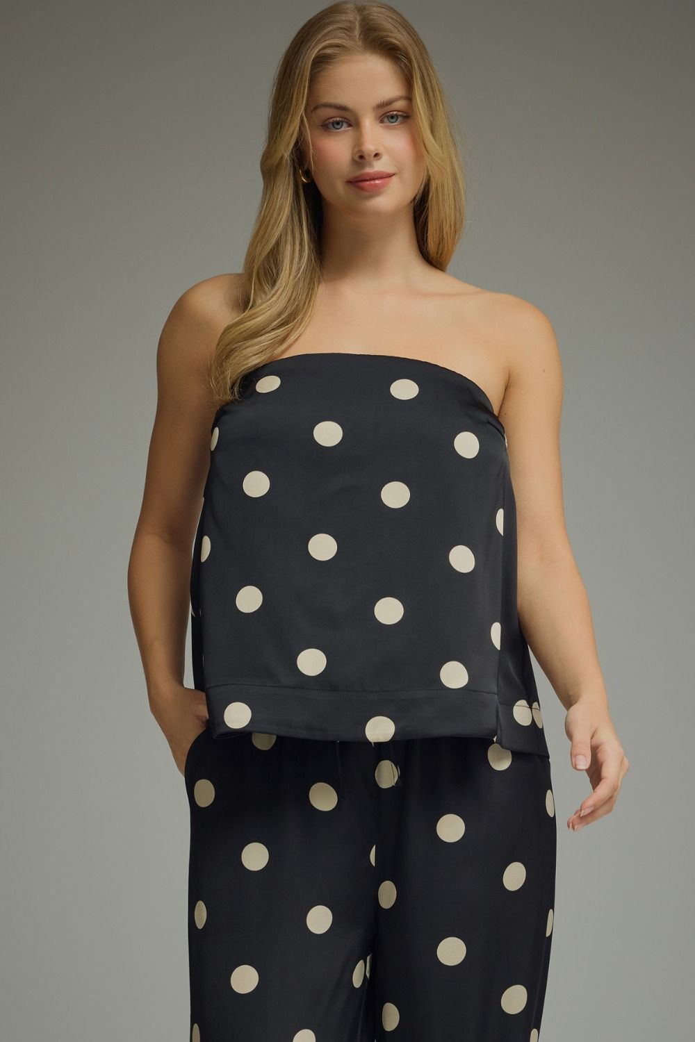 Woman wearing a black strapless top and pants with white polka dots on a gray background