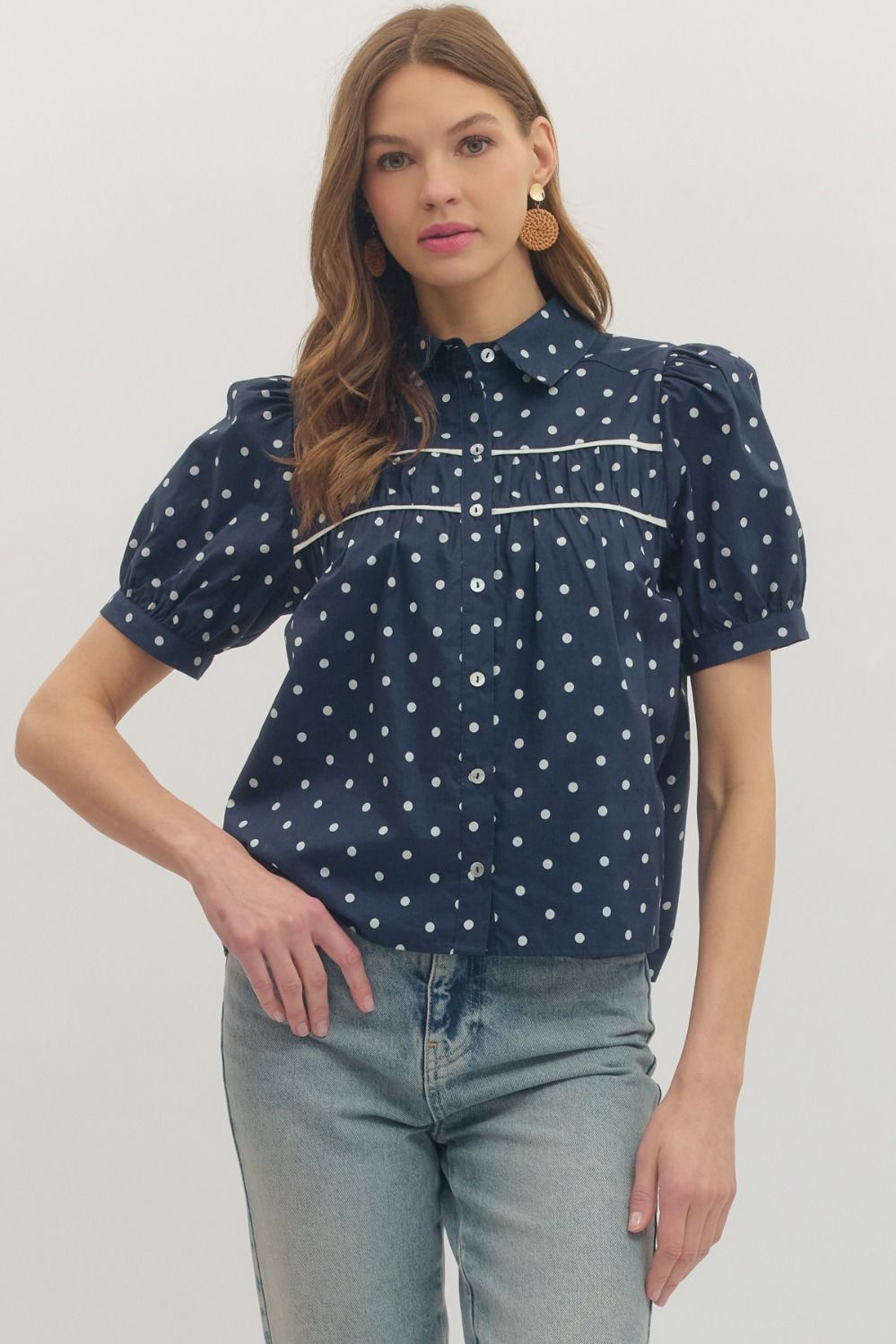 Woman wearing a navy blue blouse with white polka dots and light blue jeans on a plain background