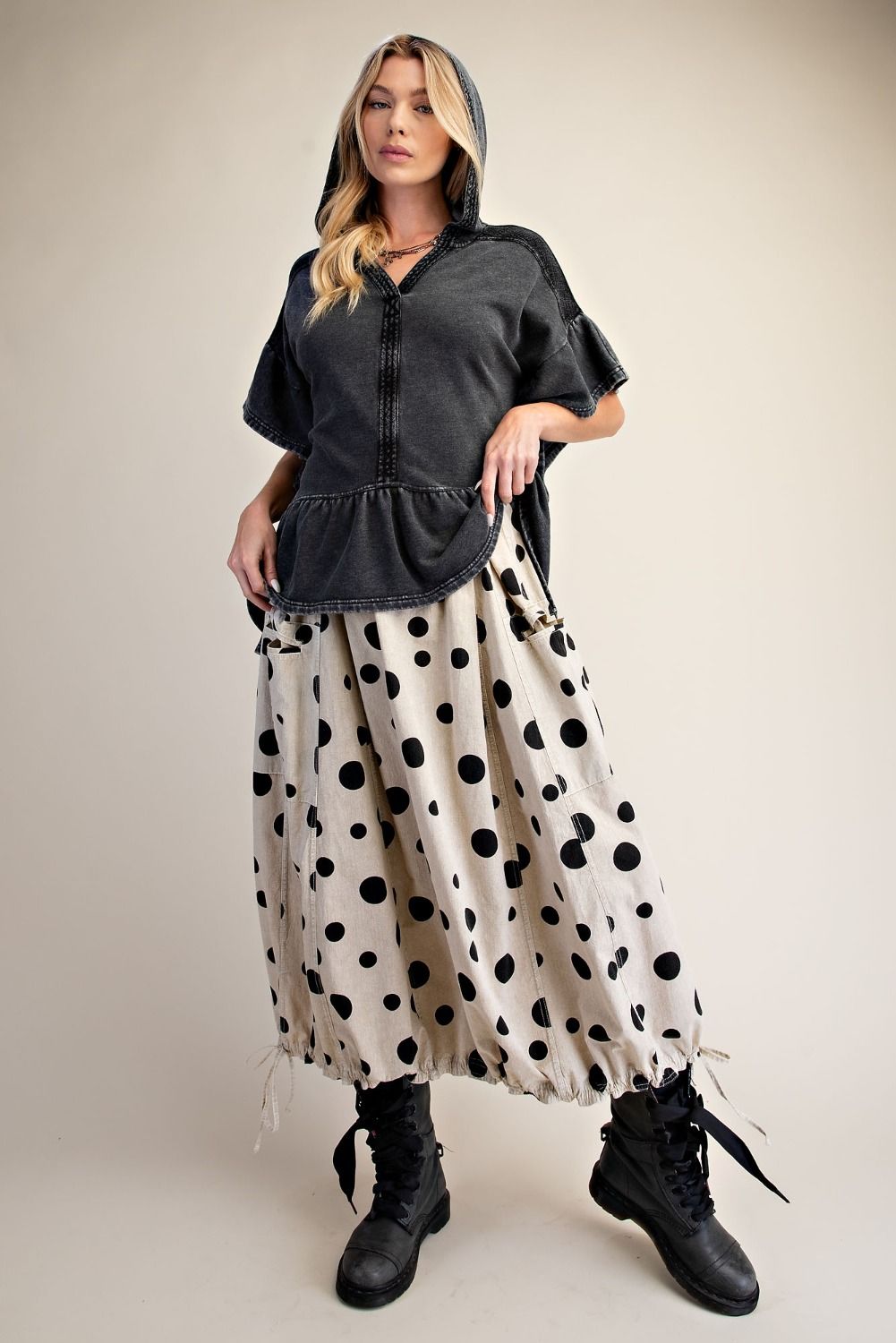 Woman wearing a black top and polka dot skirt with black boots on a beige background