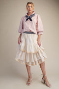 Woman wearing a pink blouse with puffed sleeves and a white ruffled skirt on a beige background