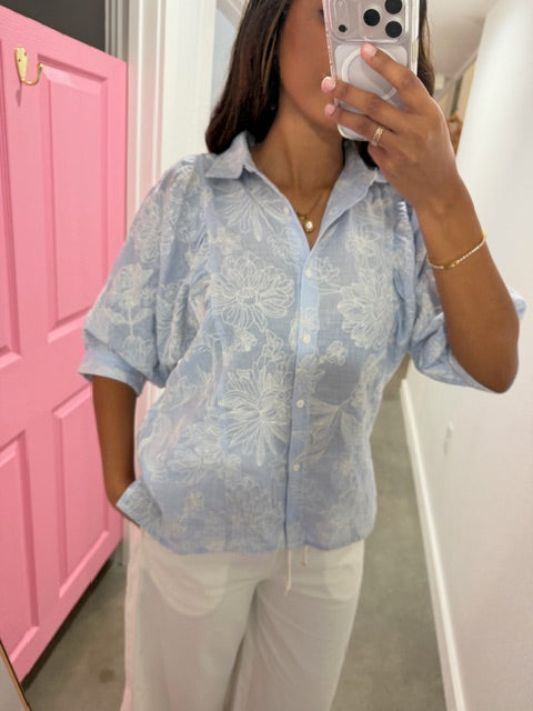 Person wearing a light blue floral blouse sitting on a pink chair.