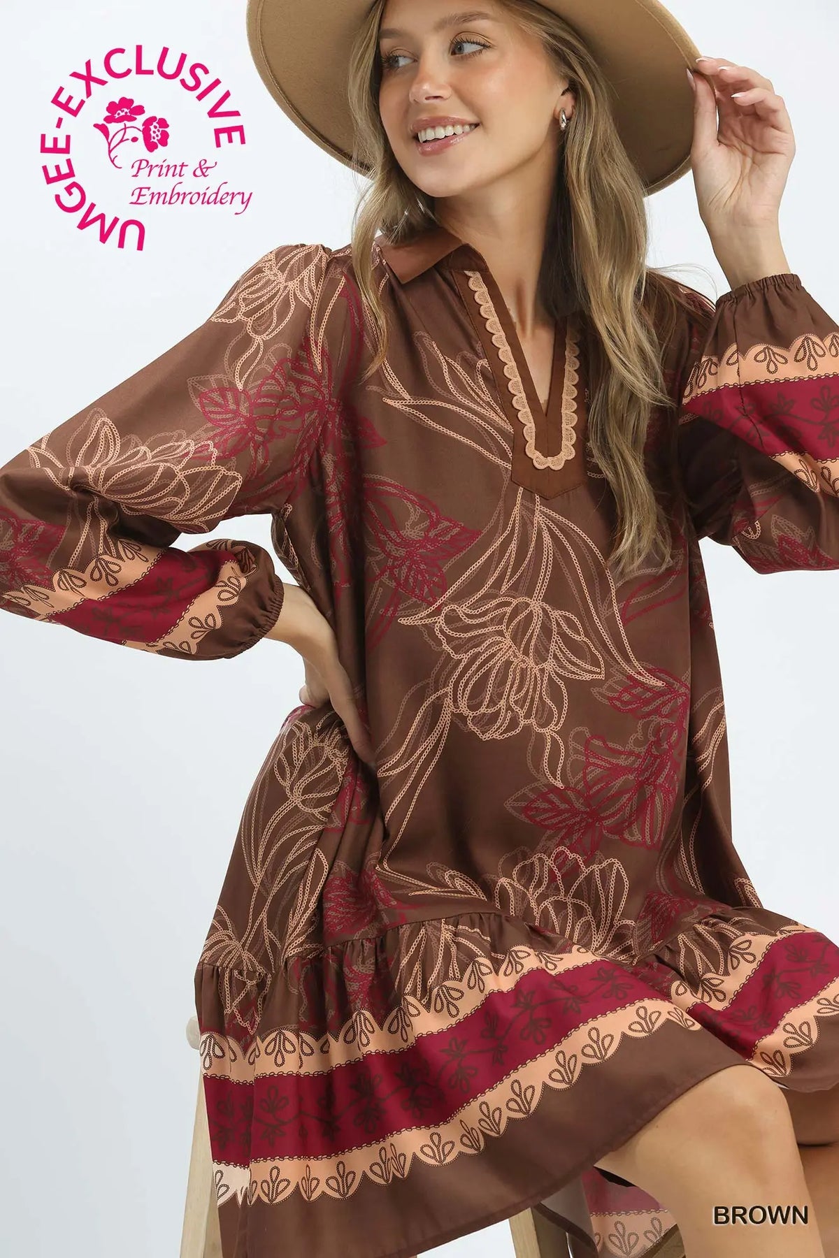 A woman wearing a brown long-sleeve dress with a beige floral pattern and red border details, styled with a tan hat against a light gray studio background. A pink 'UNIQUELY EXCLUSIVE Print & Embroidery' logo is visible in the top left, and the word 'BROWN' appears in the bottom right.