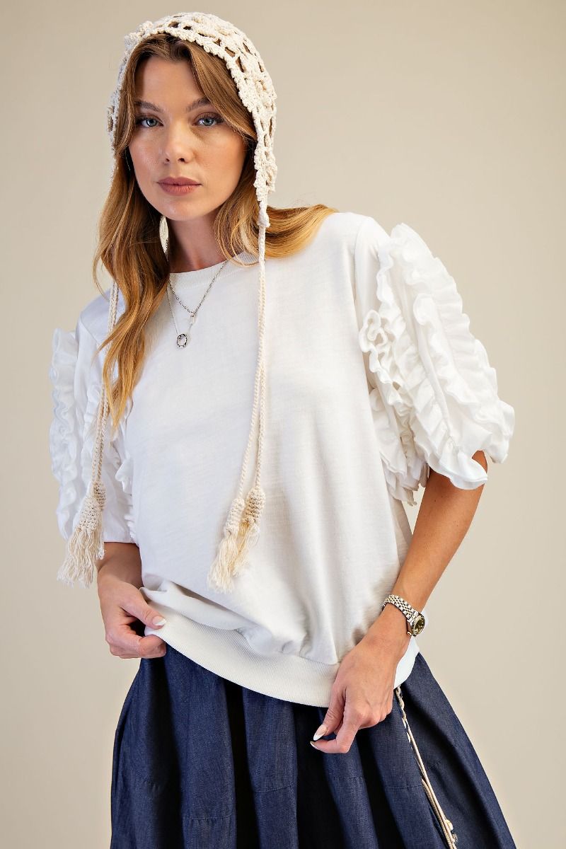 Woman wearing a white lace bonnet over her head, with a plain background
