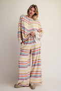 A woman modeling a matching two-piece lounge set with a pastel multicolor stripe pattern, featuring a long-sleeve top and wide-leg pants, against a plain beige studio background.