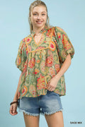 Woman wearing a colorful paisley blouse and denim shorts against a light blue background