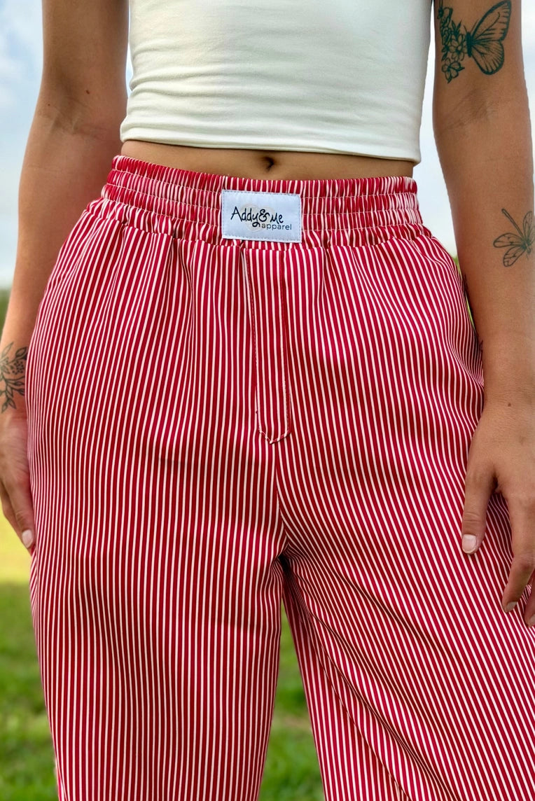 A close-up of a person wearing red and white vertically striped wide-leg pants with an elastic waistband and a visible 'All over' brand label.