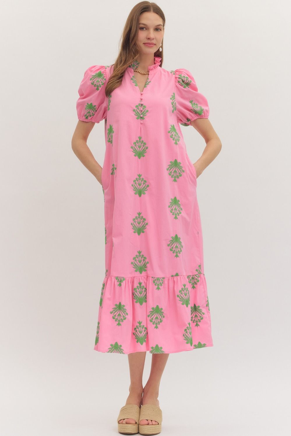 Woman wearing a pink dress with green floral patterns on a white background