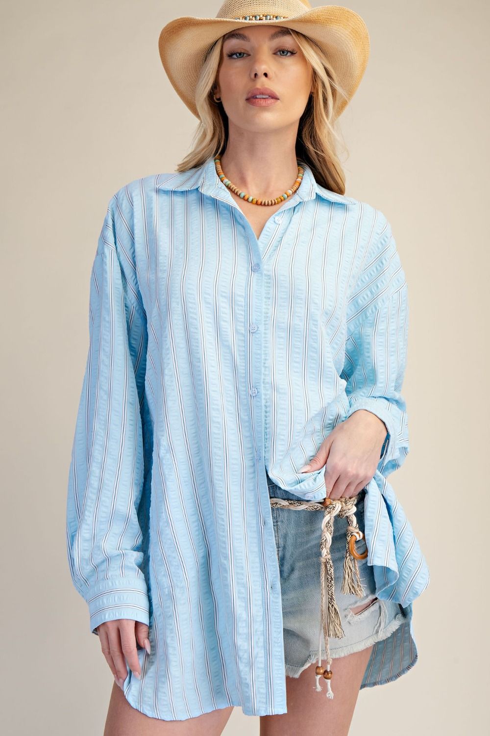 Woman wearing a light blue striped shirt and denim shorts with a beige background
