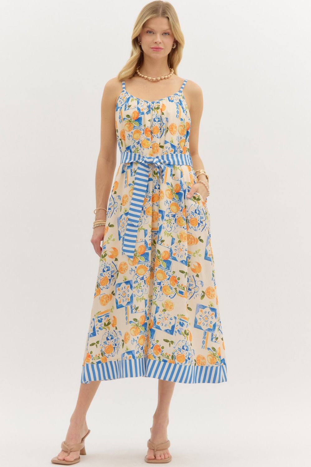 Women's sleeveless midi dress with orange fruit and tile print, belted waist, and blue striped hem – perfect summer outfit for Mediterranean vacation or resort wear