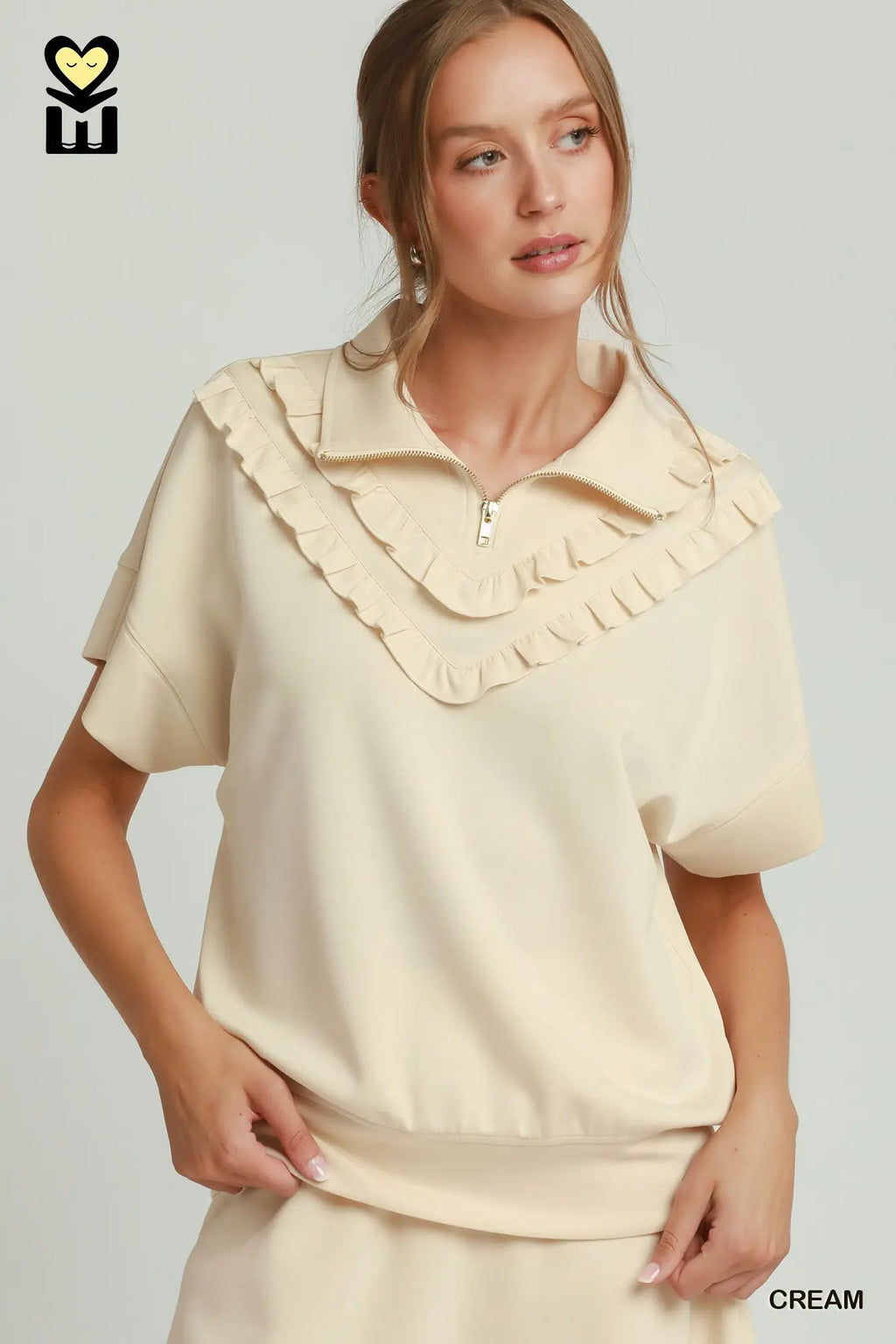 Woman wearing a cream-colored blouse with ruffled collar on a light gray background